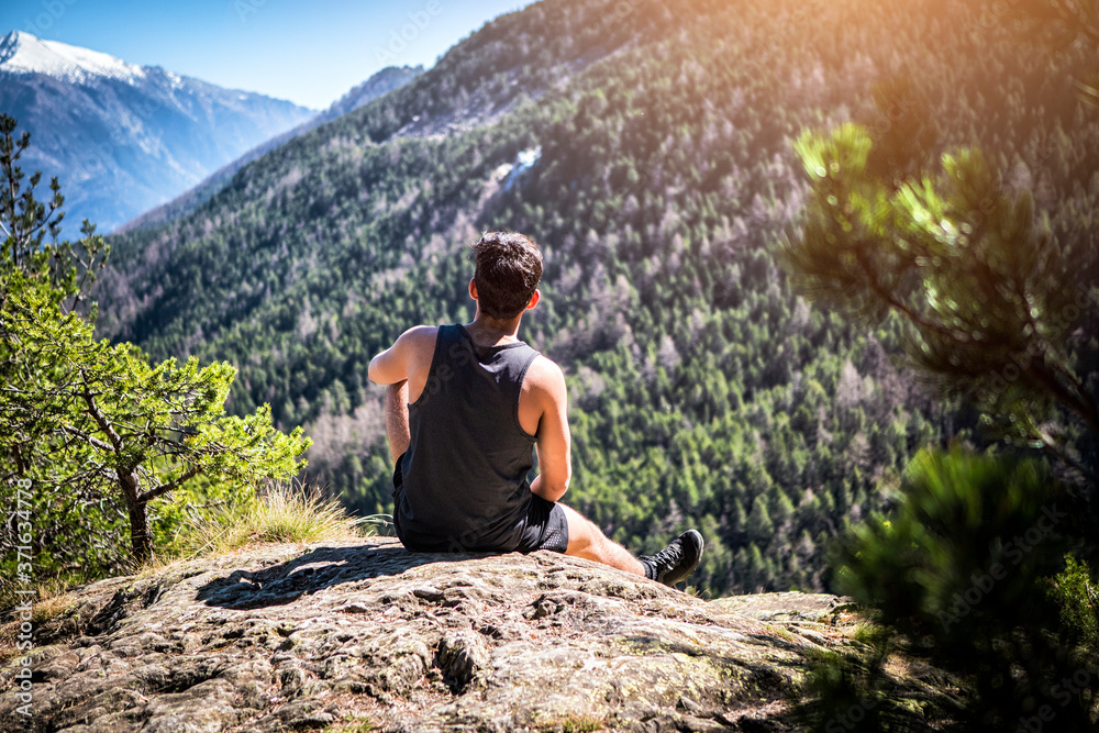 Young unrecognizable man sitting on a rock enjoying the view up the mountain in a sunny day