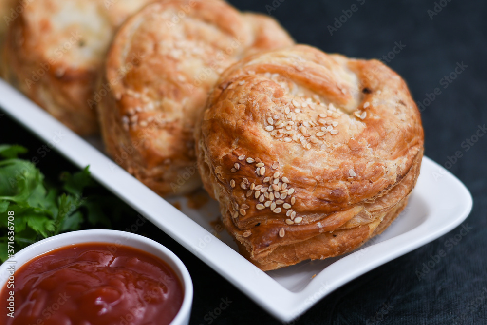 Fast food many chicken puffs, pattie pastries, popular bakery snacks with tomato sauce or ketchup in Kerala India. Indian food cut and being served using server.