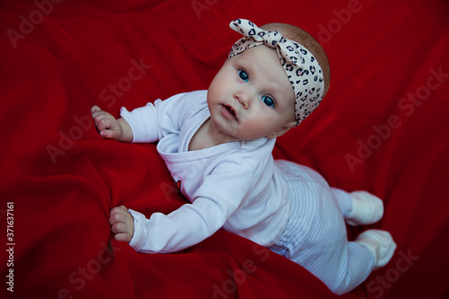 Cute happy blonde blue-eyed girl 3-4 months old lying on red blanket and looking camera. Conceptual photo for education  healthy childhood  parenting. Perfect caucasian infant. Selective focus