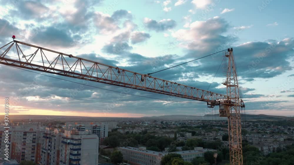 Crane against blue sky at the dusk and city horizon, industrial zone. Drone aerial shot of crane, work for the construction, high above the city. Crane against blue sky at the dusk and city horizon, industrial zone. Drone aerial shot of crane, work for the construction, high above the city.
