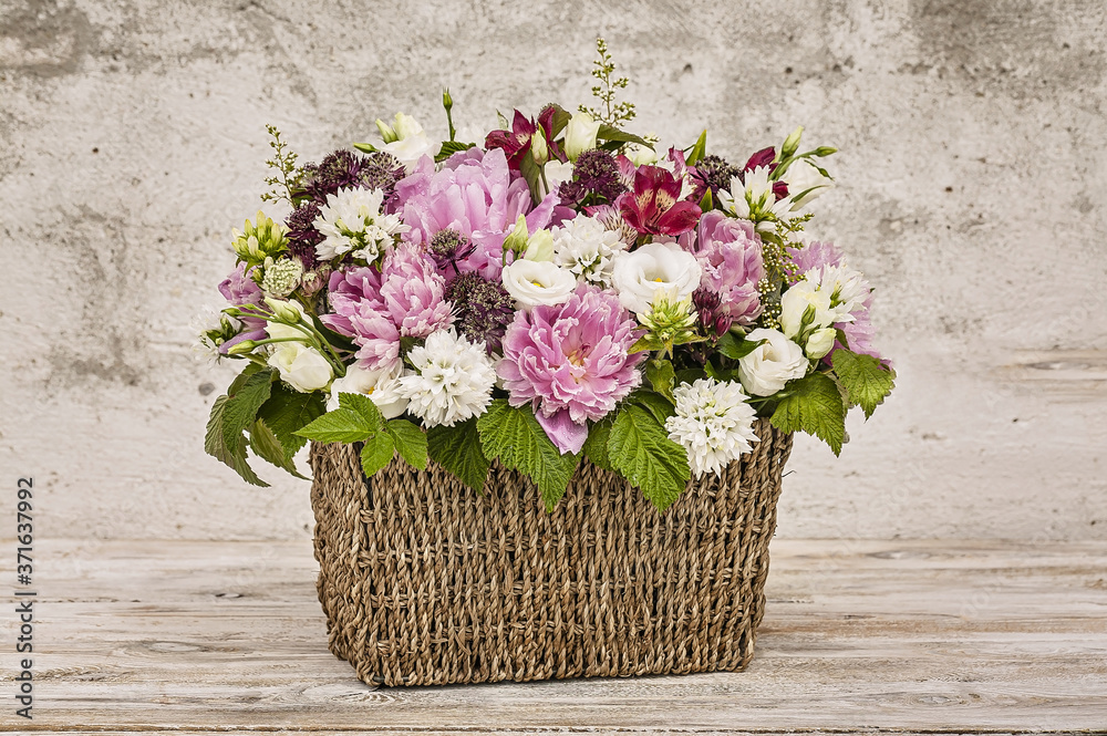 Bouquet of flowers in a basket on a gray background. Peonies, eustoma, raspberry leaves.