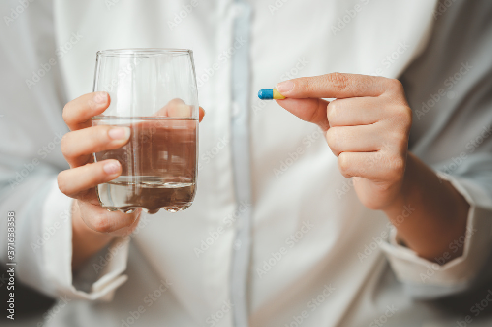 Close up shot of woman hand holding capsule pill and glass of water. Image focused on capsule Close up shot of woman hand holding capsule pill and glass of water. Image focused on capsule