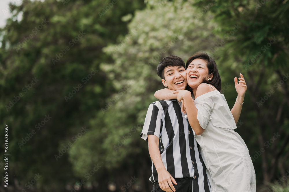 Happy Asian lesbian LGBT couple in love hugging while laugh and smile together in the park