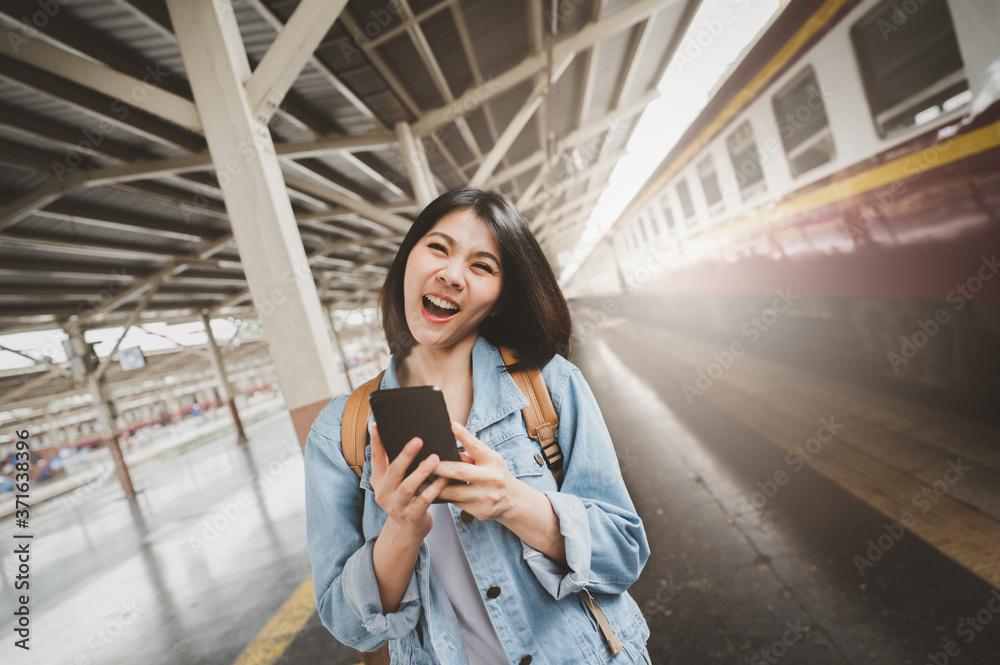 Fototapeta premium Happy smiling Asian woman tourist travel with backpacker holding smartphone at train station platform