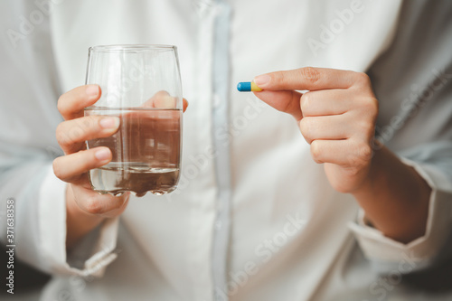 Close up shot of woman hand holding capsule pill and glass of water. Image focused on capsule