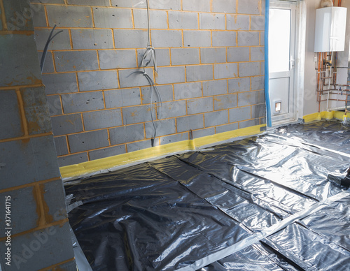 Preparation stage of laying of underfloor heating, the layer of plastic over insulated floors, protected windows, block walls in residential extension building project, selective focus photo