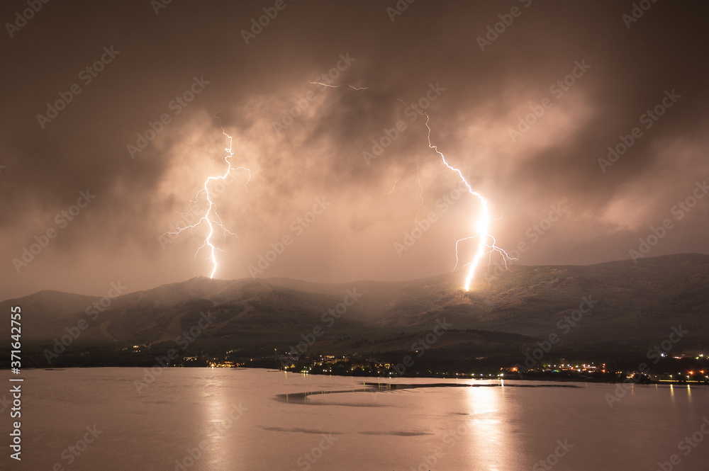 Scenery lightning strike during rainy storm hitting the mountain near lake