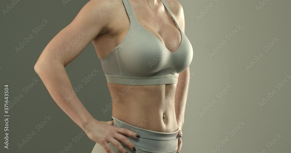 Close-up of sportswoman torso in sports bra, female fitness intructor, showing abs and perfect body, workout in gym. Fit body of young woman with muscles and biceps over studio background