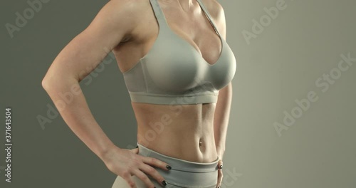 Close-up of sportswoman torso in sports bra, female fitness intructor, showing abs and perfect body, workout in gym. Fit body of young woman with muscles and biceps over studio background