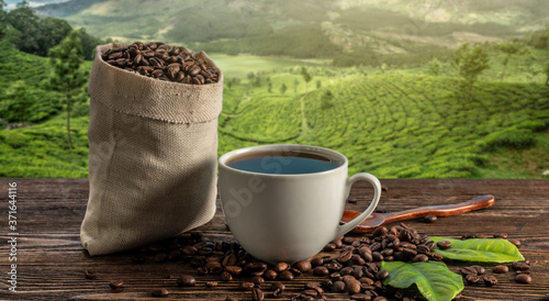 A Cup of fresh coffee and roasted beans in a bag on the table against the backdrop of a landscape of coffee plantations