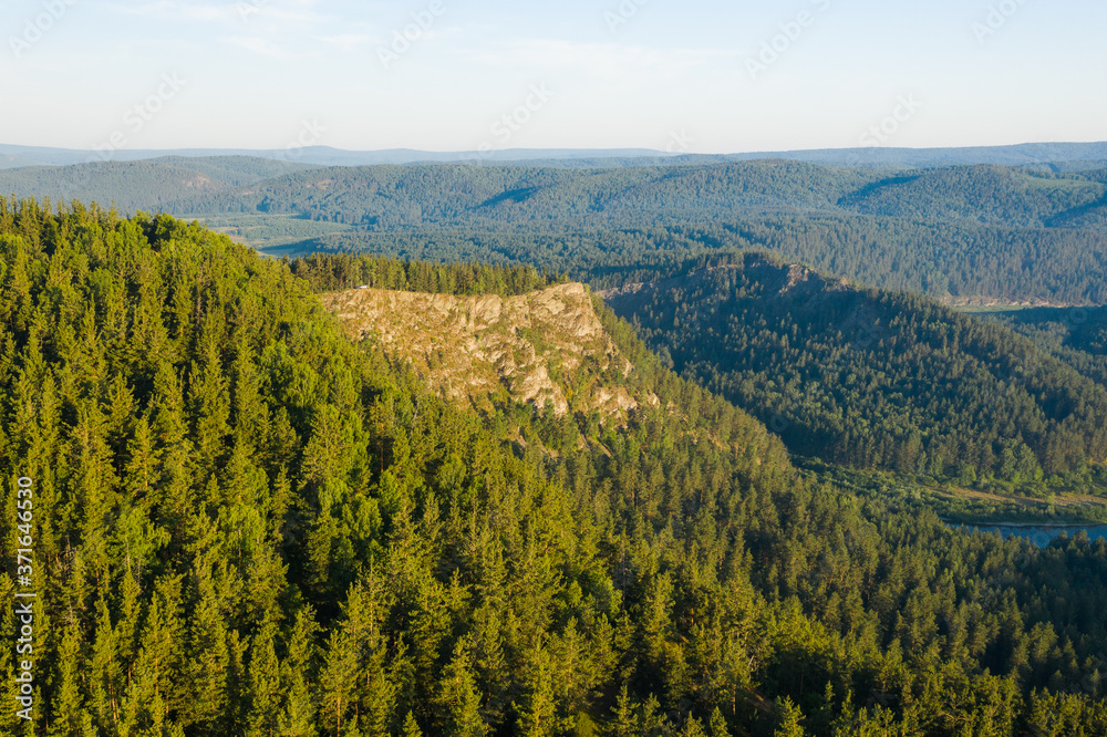 Fototapeta premium Bare rock among green mountains covered by pine trees forest in Ural, Bashkortostan, Russia
