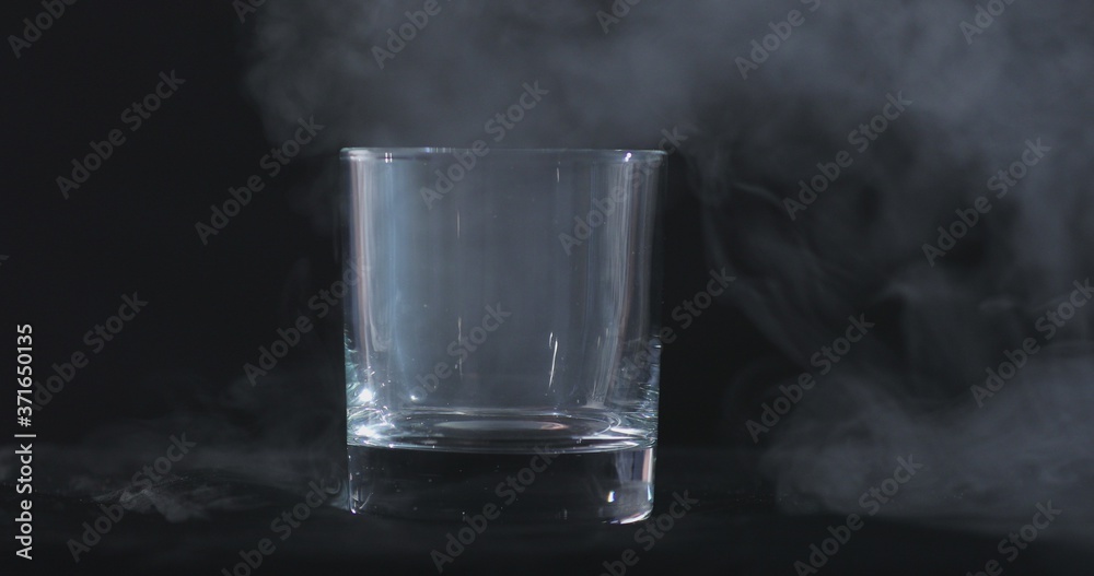 An empty whiskey, alcohol glass against a black background and floating smoke An empty whiskey, alcohol glass against a black background and floating smoke