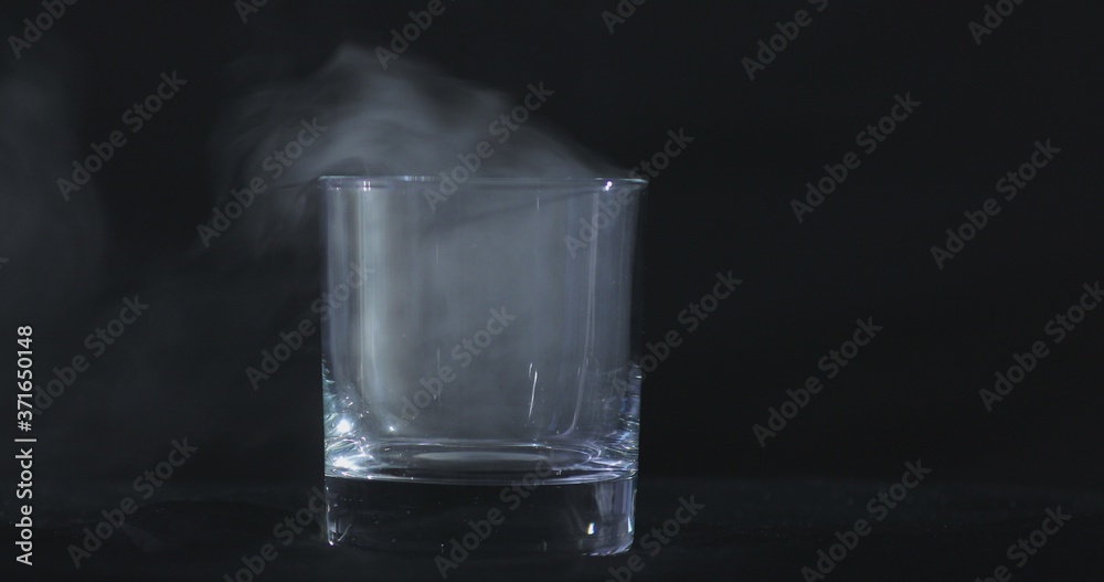 An empty whiskey, alcohol glass against a black background and floating smoke An empty whiskey, alcohol glass against a black background and floating smoke