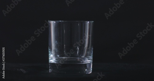 An empty whiskey, alcohol glass against a black background and floating smoke