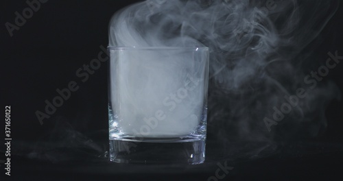 An empty whiskey, alcohol glass against a black background and floating smoke