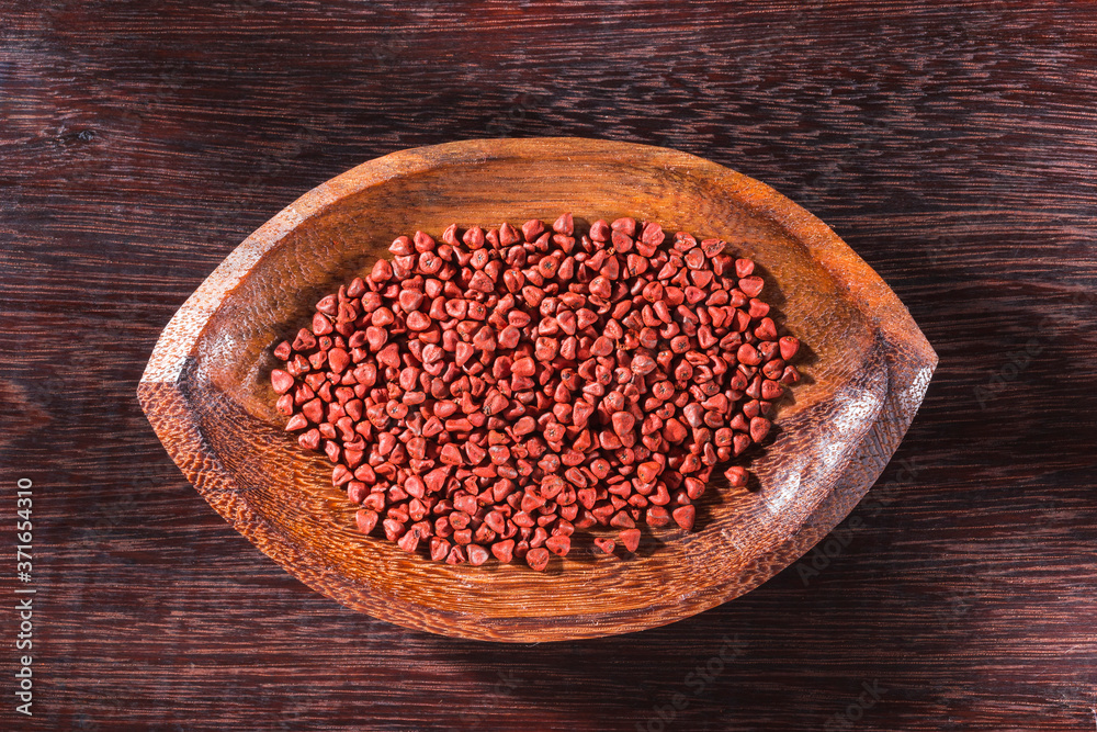 Annatto seeds in bowl on wooden background - Bixa Orellana. Annatto seeds in bowl on wooden background - Bixa Orellana.