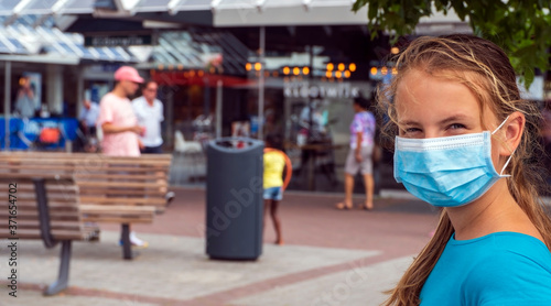A young girl wears a face mask on the streets of the city.Cute Teenage Girl with a surgical mask on her face that protects against the spread of coronavirus disease.