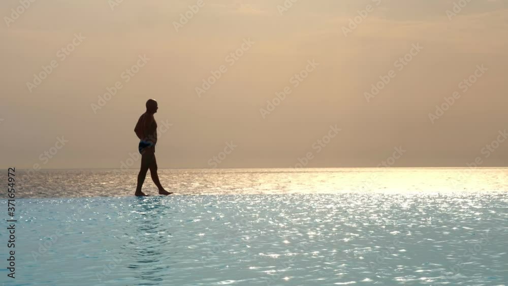 dark silhouette, man walking on edge of outdoor infinity pool with panoramic sea view, at sunrise. inspiration, travel and vacation concept dark silhouette, man walking on edge of outdoor infinity pool with panoramic sea view, at sunrise. inspiration, travel and vacation concept