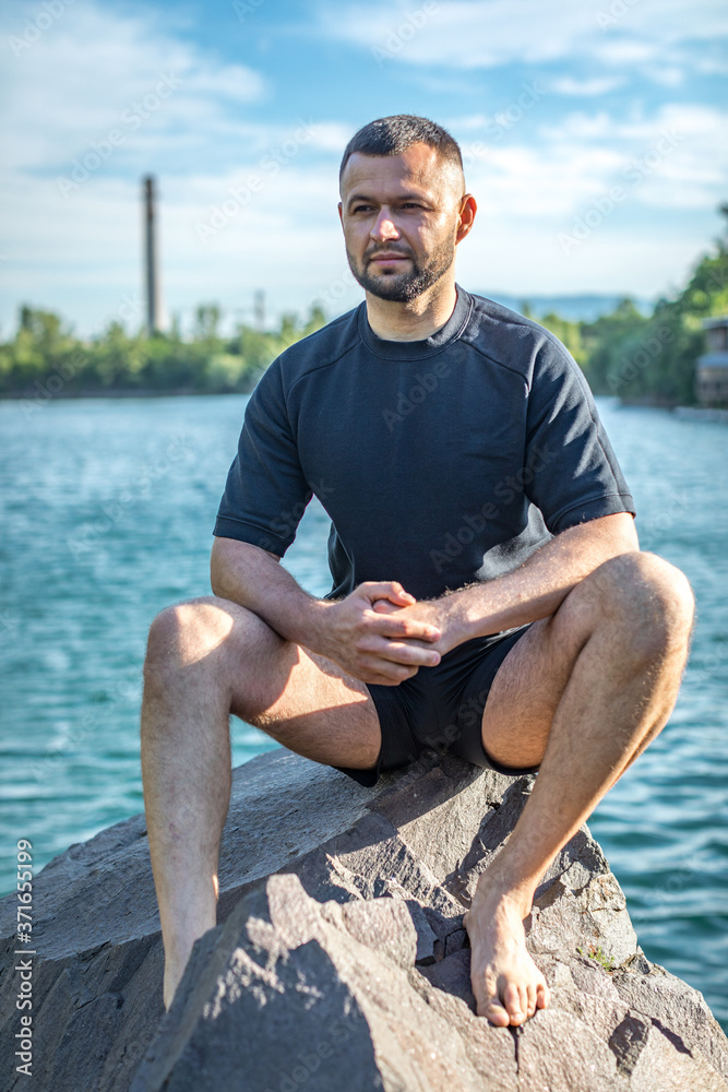 Bearded young man sitting on the rocks on the quarry lake background. Handsome portrait.