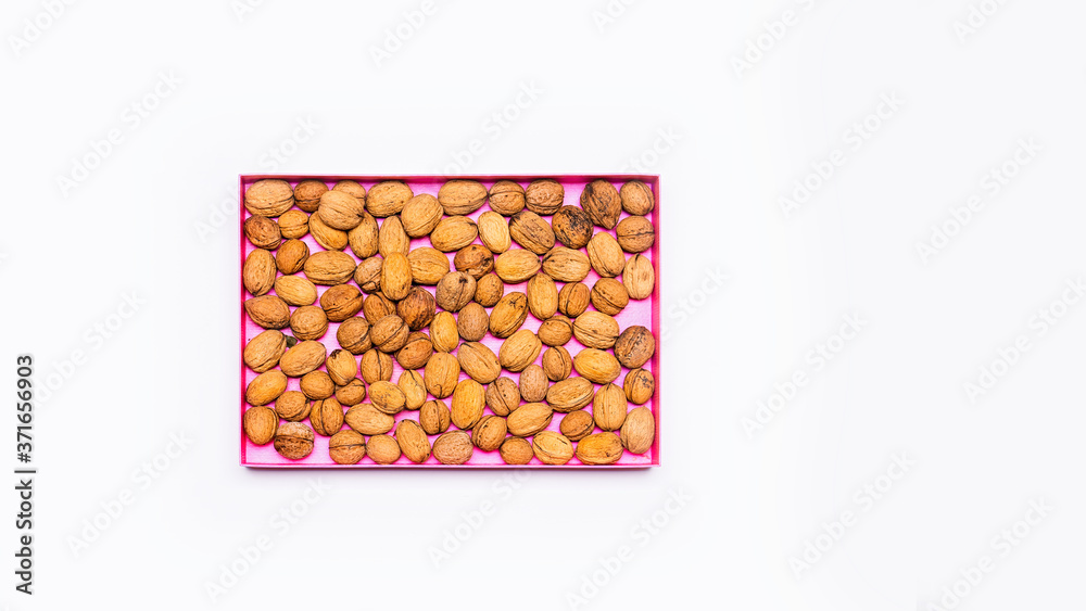 Natural walnuts stacked in a pink box. Everything is arranged on a bright table. Flat, top view, no people. Natural walnuts stacked in a pink box. Everything is arranged on a bright table. Flat, top view, no people.