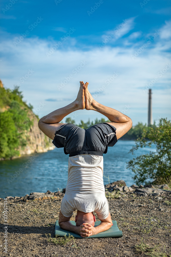 Strong healthy athletic man doing morning workout, practicing yoga at the quarry lake, standing on hand upside down. Relaxe and meditation, healthy lifestyle concept. International Day of Yoga.