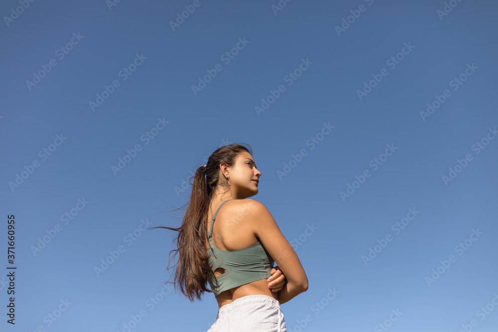 Obraz premium Confident sporty young fit woman. Fitness motivation and success concept. Female motivated runner isolated on blue clear sky.