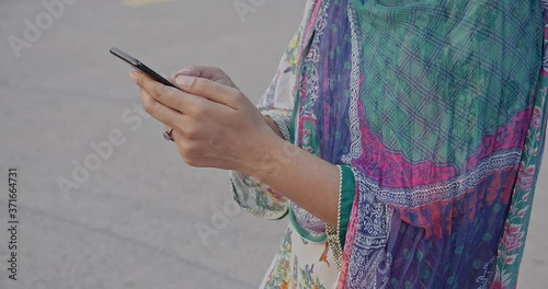 Women using cell phone while standing in a traditional Pakistani kameez shalwar dress