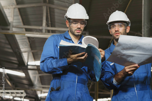 Factory Engineer or mechanical worker with white safety helmet holding the manual and consulting on production in a factory. Industrial,Warehouse Heavy Mechanic, Problem, Engineering Concept. 
