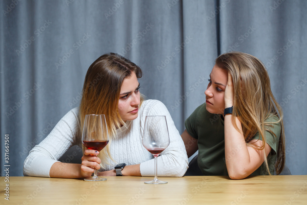 Two happy young women are friends with wine enjoying a conversation in the living room at home. girls roommate chatting at the table. European women relax talking in a cozy house. Two happy young women are friends with wine enjoying a conversation in the living room at home. girls roommate chatting at the table. European women relax talking in a cozy house.