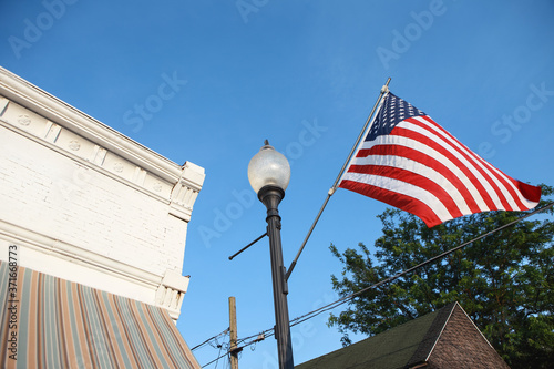 Fototapeta Naklejka Na Ścianę i Meble -  American flag flying in a small town on main street in the USA