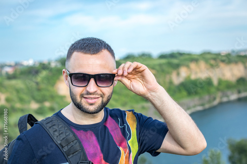 Happy bearded man standing outdoors during sunny spring day at quarry lake.