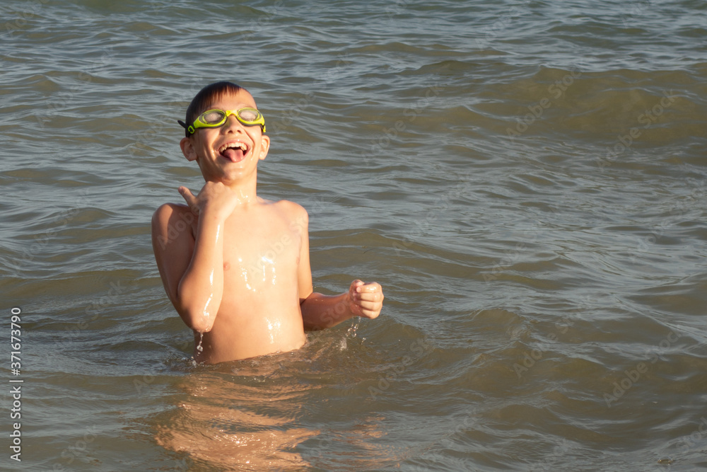 A 10-year-old boy is swimming and having fun in the sea near the shore in green swimming goggles. A 10-year-old boy is swimming and having fun in the sea near the shore in green swimming goggles.