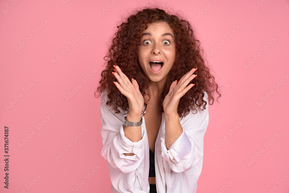 Woman cannot calm down from super happiness. Attractive cheerful redhead girlfriend shining from positive emotions, holding hands near face, dropping jaw from surprise, excited over pink wall Woman cannot calm down from super happiness. Attractive cheerful redhead girlfriend shining from positive emotions, holding hands near face, dropping jaw from surprise, excited over pink wall