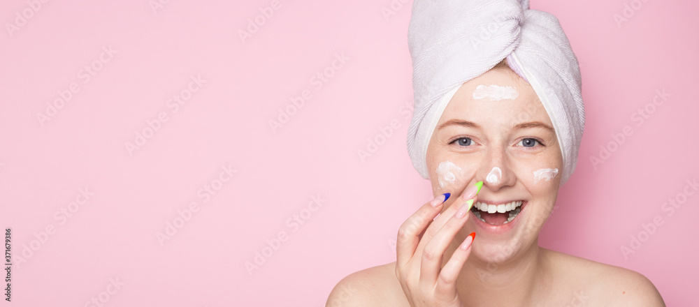 Smiling woman with a towel on her head on a pink background and face cream. Hydration of the skin, skin care face, beauty. Smiling woman with a towel on her head on a pink background and face cream. Hydration of the skin, skin care face, beauty.