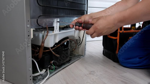 Worker repairing refrigerator in kitchen, closeup