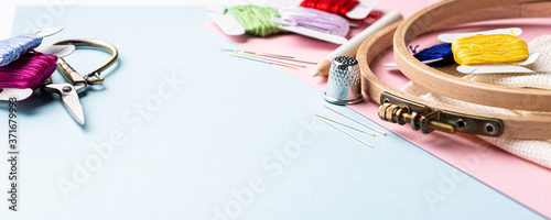 Embroidery set fot cross stitching. White fabric, embroidery hoop, colorful threads, scissors and needls. On blue background. Hobbies concept with copy space. Banner