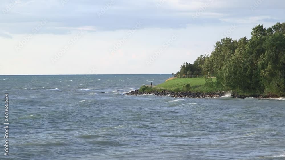 Scenic shoreline with bikers on a path. Windy day and big waves crashing. Wide static. Lake Huron. Scenic shoreline with bikers on a path. Windy day and big waves crashing. Wide static. Lake Huron.