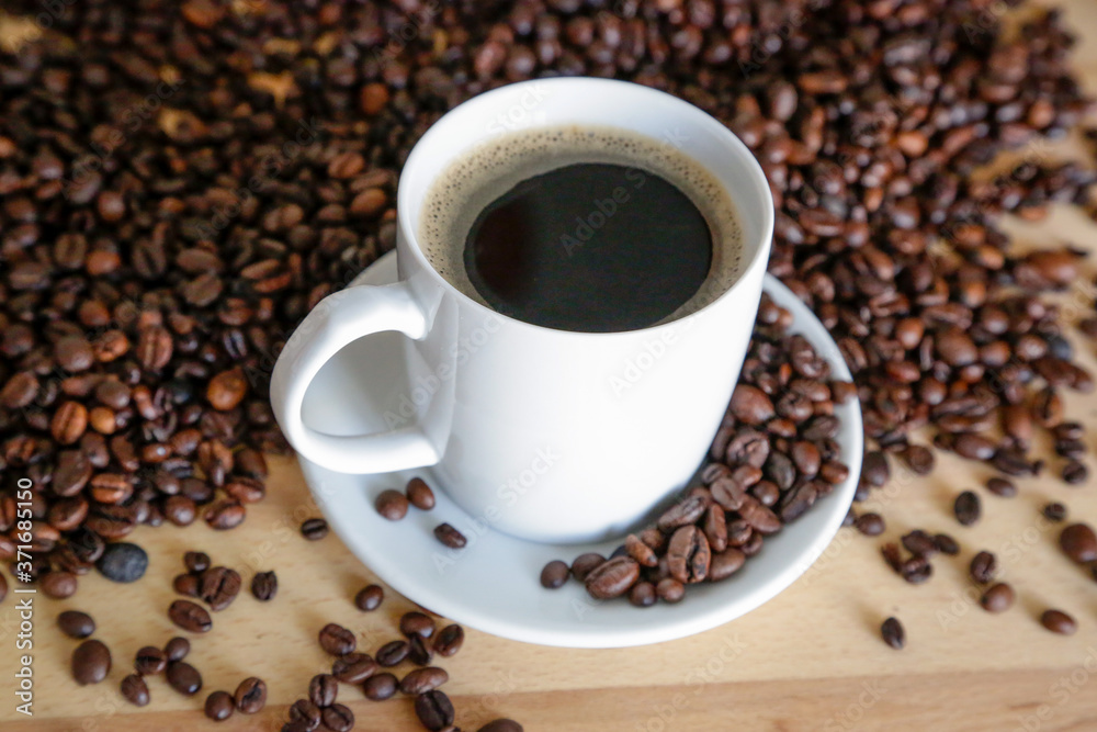 A cup of black coffee with coffee grains, natural light on wooden table A cup of black coffee with coffee grains, natural light on wooden table