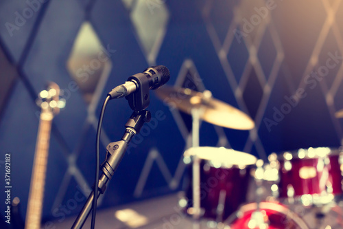 Selective focus to microphone with blurry rock band, drum set, solo guitar on stage.