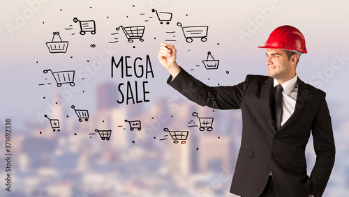 Handsome businessman with helmet drawing MEGA SALE inscription, contruction sale concept