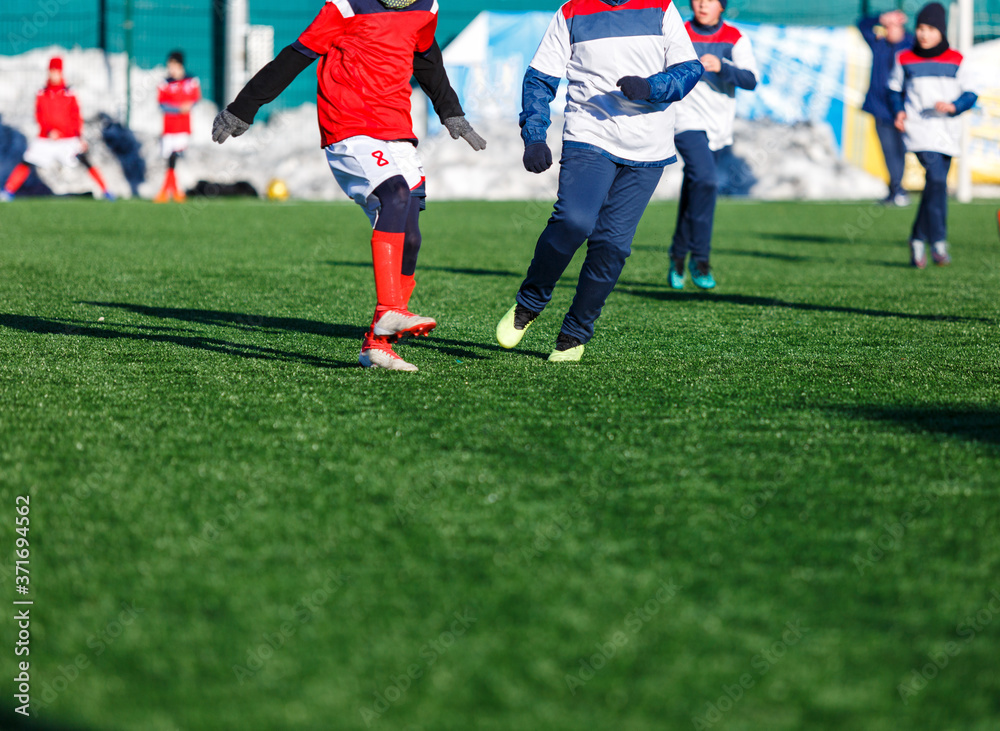 Boys in white red sportswear running on soccer field with snow on background. Young footballers dribble and kick football ball in game. Training, active lifestyle, sport, children winter activity Boys in white red sportswear running on soccer field with snow on background. Young footballers dribble and kick football ball in game. Training, active lifestyle, sport, children winter activity