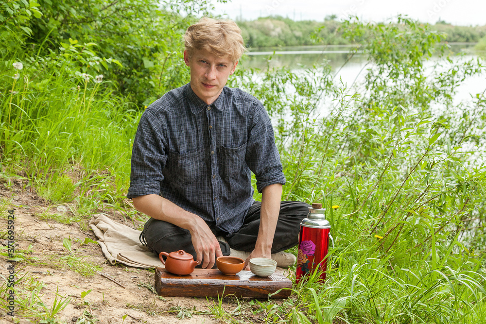 Young man with blonde hair drinking chinese tea in summer park Young man with blonde hair drinking chinese tea in summer park