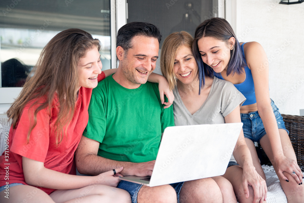 Happy Family With Two Daughters Using Laptop Together. Sitting on a Sofa at the Balcony Happy Family With Two Daughters Using Laptop Together. Sitting on a Sofa at the Balcony