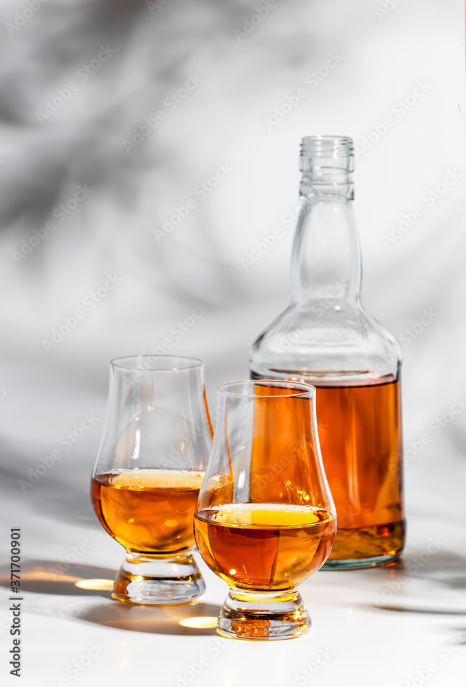 Scotch Whiskey without ice in glasses and bottle, white background with hard light, shadows and sun glare, copy space Scotch Whiskey without ice in glasses and bottle, white background with hard light, shadows and sun glare, copy space