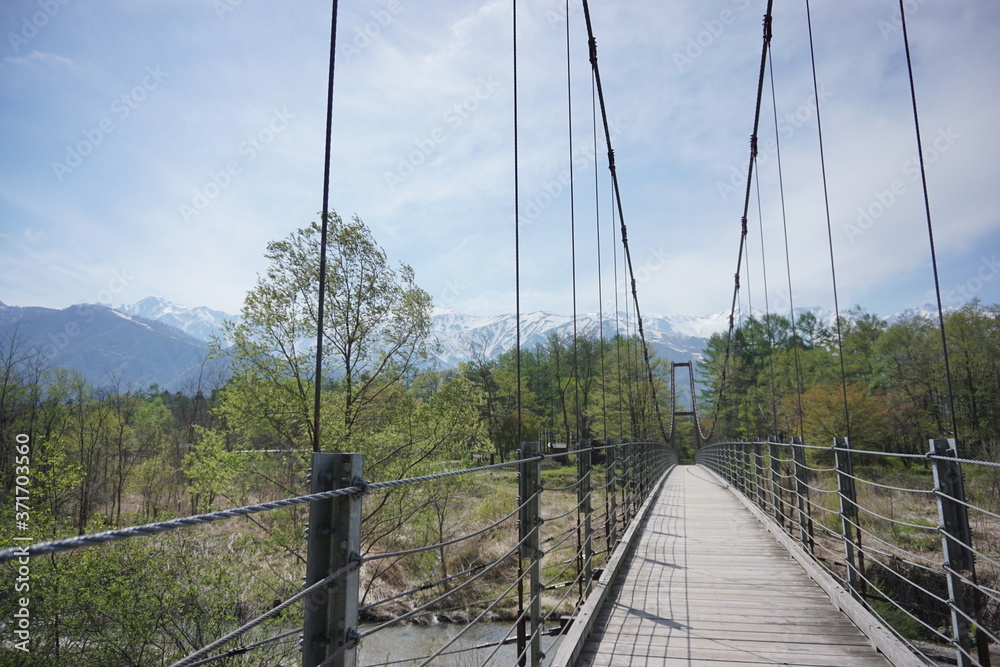 Obraz premium Wooden bridge over the river and beautiful summer landscape of Japanese alps in Hakuba, Japan