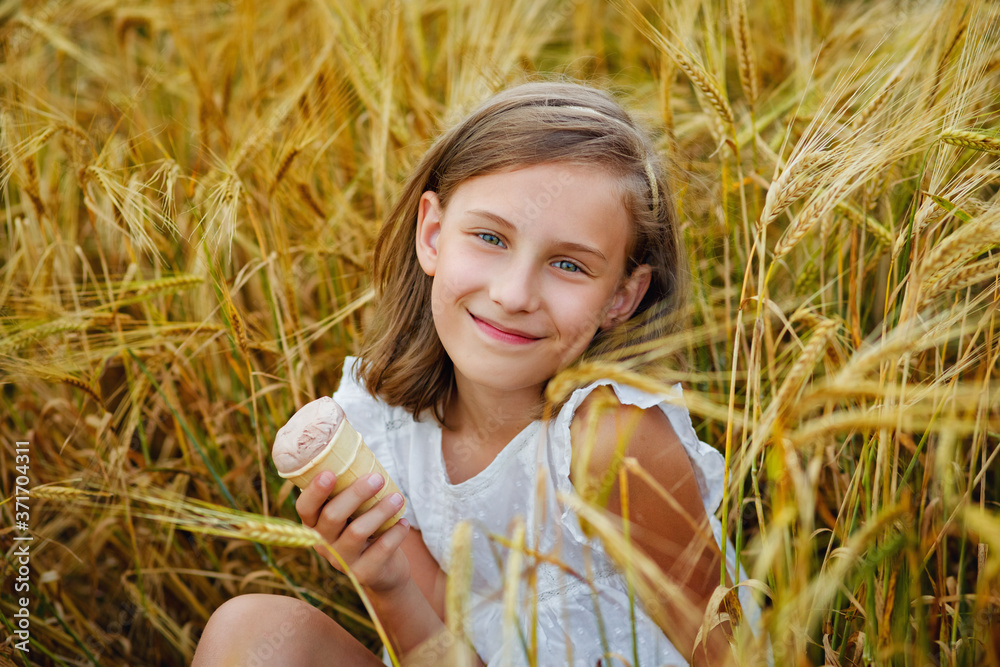 A beautiful smiling girl with ice cream in her hands is sitting and eating at a picnic in a wheat field. A beautiful smiling girl with ice cream in her hands is sitting and eating at a picnic in a wheat field.