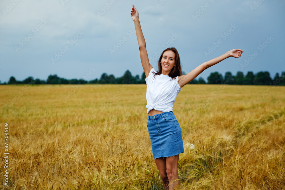 A thin, laughing girl stands with her arms outstretched in the middle of a wheat field against a cloudy sky. A thin, laughing girl stands with her arms outstretched in the middle of a wheat field against a cloudy sky.