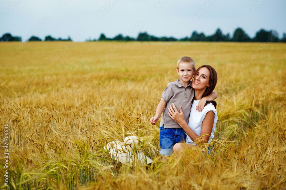Happy family mom and son in a summer wheat field. A young woman hugs her son.