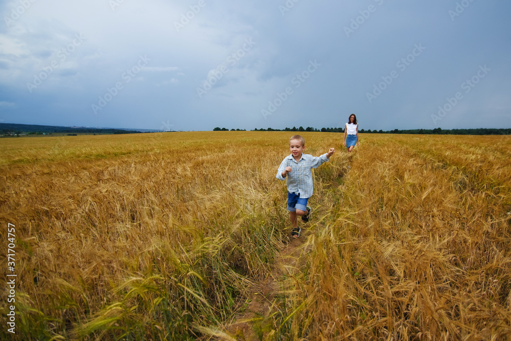 Happy family mother and son in a summer wheat field. The boy runs merrily across the field.