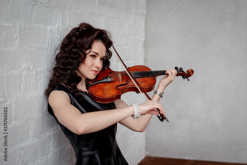 Young attractive brunette girl of Asian appearance on a white brick background with a violin in her hands. Young attractive brunette girl of Asian appearance on a white brick background with a violin in her hands.